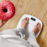 Diyet. Tartıda Vücut Ağırlığını Ölçen Kadın Donut Tutuyor. Tatlılar Sağlıksız Abur Cuburlardır.